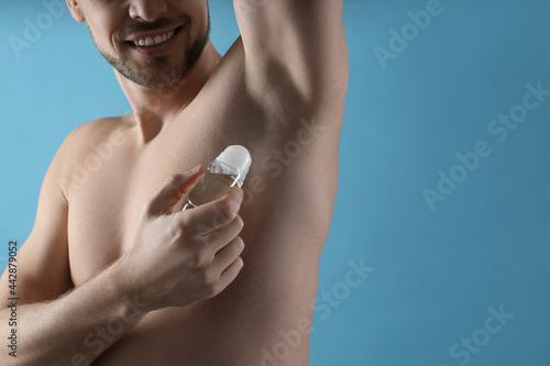 Man applying deodorant on turquoise background, closeup. Space for text