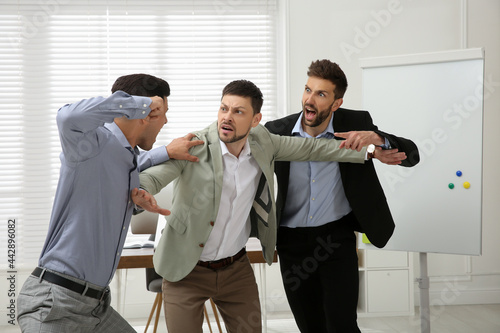 Man interrupting colleagues fight at work in office