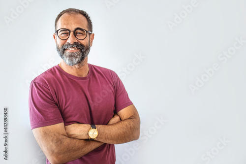 Portrait of happy mature man wearing spectacles and looking at camera indoor. Man with beard and glasses feeling confident. Handsome mature man posing against a grey background