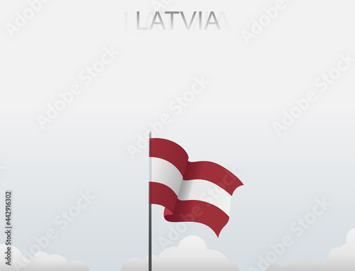 Latvian flag flying on a pole standing tall under a white sky