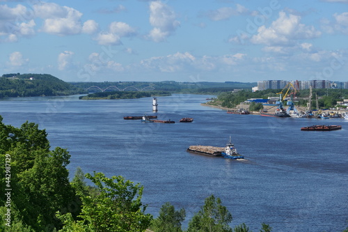 Nice view of the river. A tugboat with a barge loaded with wooden logs is sailing along the river. . High