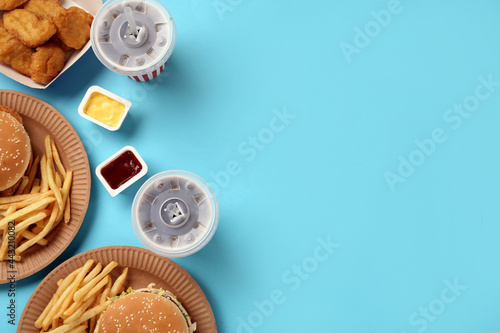 Different fast food on turquoise background, flat lay. Space for text