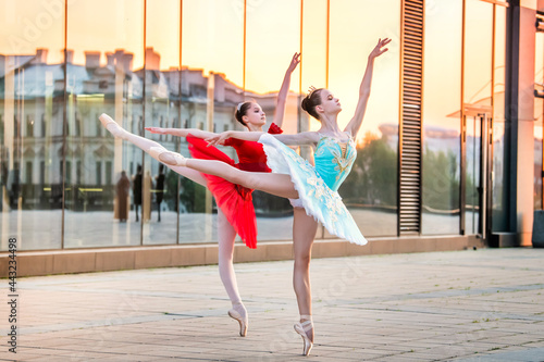 two young ballerinas in a bright red and blue tutu are dancing against backdrop of the reflection of city sunset