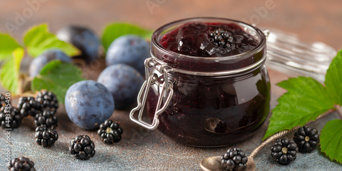 Blackberry and plum jam preserves in a jar and fresh berries on the table.