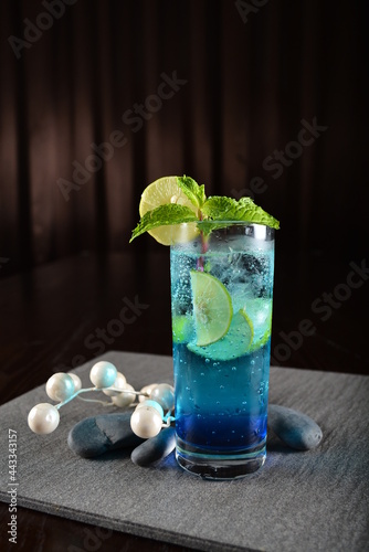 iced blue island cooler soda mocktail with lime and mint leaf kombucha in glass on bar counter dark night background restaurant hotel luxury cafe pub beverage cold halal bar drink menu