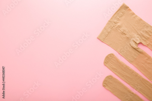 New brown nylon female pantyhose on light pink table background. Pastel color. Closeup. Empty place for text or logo. Top down view.