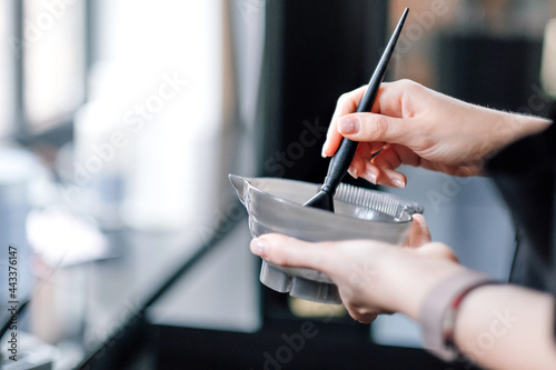 Hairdresser holding bowl with hair dye in beauty salon