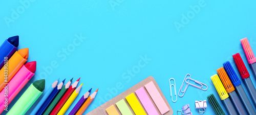 Wide banner. Colorful pencils, felt-tip pens, brushes, stickers and stationery flat lay. School office supplies lie from below on light blue background. Back to school and new academic year concept.