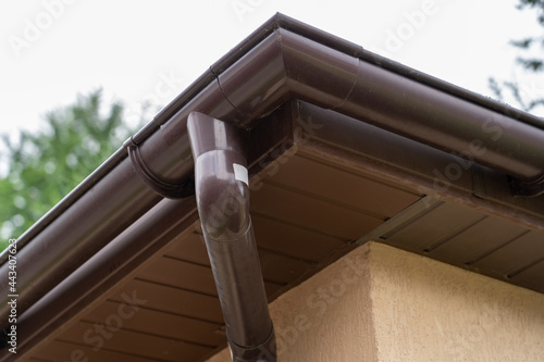 Brown plastic gutter system against sky, roof overhang