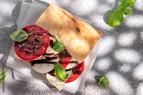Delicious sandwich with caprese salad. Ripe tomatoes and mozzarella cheese with fresh basil leaves. Italian food.