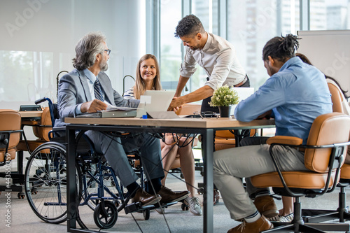 Happy businessman in wheelchair reading documents during a meeting with his colleagues in the office. Shot of a team of businesspeople having a meeting in a modern office