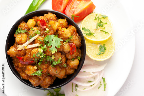 Chickpeas masala (Spicy chola or chhole curry) garnished with fresh green coriander and ingredients. Served in a black bowl. A Classic Indian typical Panjabi street food. In white background