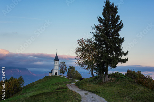 Scenic view of Jamnik church St Primus and Felician at sunset, Alps mountains, Slovenia. Beautiful landscape with footpath and sky with clouds, outdoor travel background, famous tourist attraction