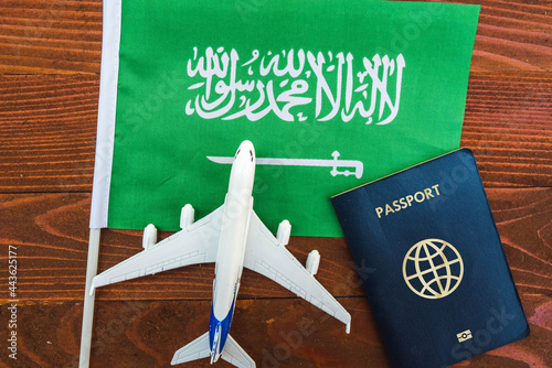 Flag of Saudi Arabia with passport and toy airplane on wooden background. Flight travel concept 