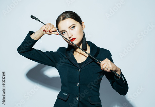 Young beautiful dominant lady posing in black outfit and holding a whip