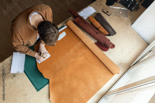 Male tanner making cutting scheme of bag working at leather workshop. Handcrafted creating