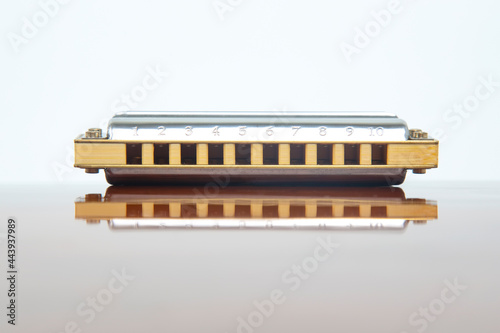 The harmonica lies on a mirrored surface. Classical musical wind instrument.