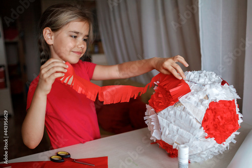 Preteen girl doing pinata with cardboard from used box and color crepe paper, decorated container filled with candy as a part of celebration, diy decoration at birthday, soccer party, focus on hand
