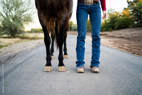 perspective of horse hooves and a woman's feet with cowboy boots standing side by side
