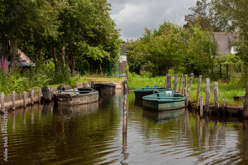 Quatre barques sont attachées sur des piquets en bois dans le marais de Brière en France. Des arbres entourent le petit port.