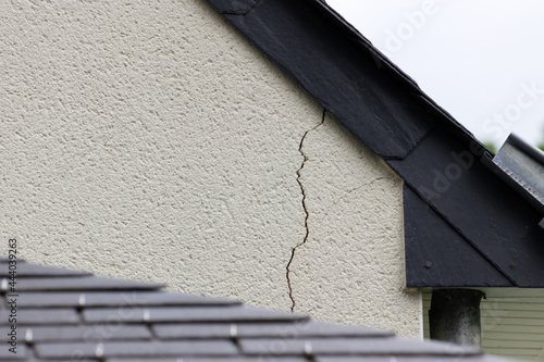 Fissure importante dans l'enduit d'un mur de maison juste sous la toiture en ardoise