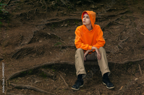 sad teenager in a hoodie sits on a natural background