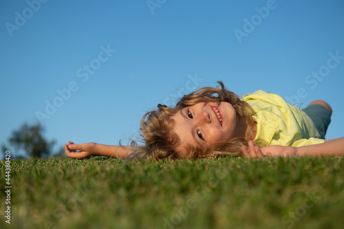 Kid playing in the meadow. Happy healthy caucasian child boy with lying on the grass field background. Little child in beautiful green environment. Amazing happy kids outdoor.
