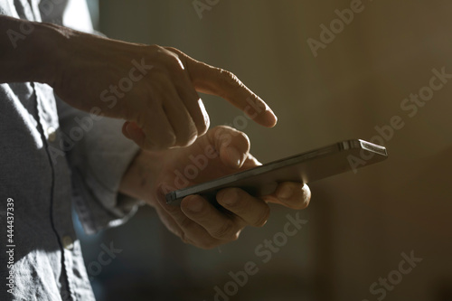 Close-up of man using mobile phone for searching information in internet. Persons hand holding smartphone on dark background.