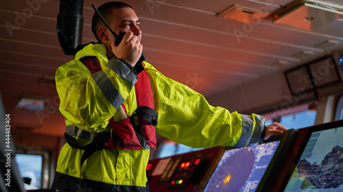 Navigator. pilot, captain as pat of ship crew performing daily duties with VHF radio, binoculars on board of modern ship with high quality navigation equipment on the bridge on sunrise.