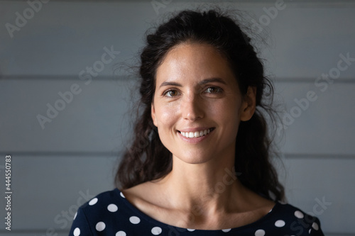 Portrait of happy pretty Hispanic 30s woman with black wavy hair looking at camera. Beautiful female model with toothy smile posing against grey background. Head shot, profile picture