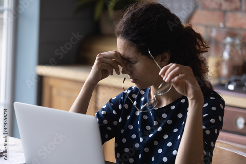 Tired woman working from home, using computer too long, taking off glasses, touching head and eyelids with closed irritable eyes. Remote employee suffering from bad vision, eyesight problems