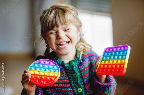 Little blonde preschool girl playing with new trend sensory toy - rainbow pop it. Antistress toy for children and adult. Colorful toy simple dimple. Squishy soft bubble toys rainbow color. Happy child