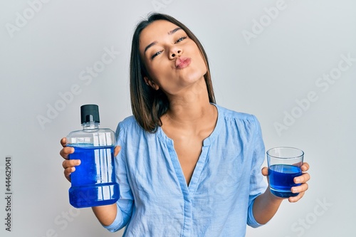Young hispanic girl holding mouthwash for fresh breath looking at the camera blowing a kiss being lovely and sexy. love expression.