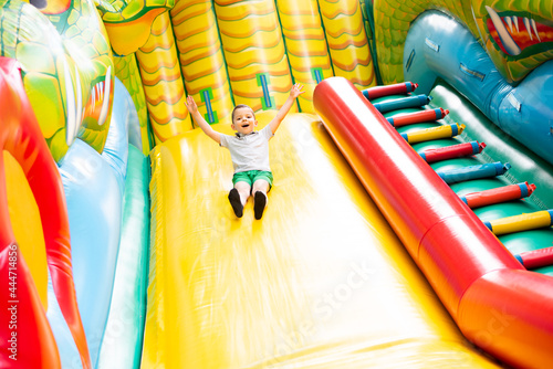Little boy child rides on an inflatable multi-colored slide.