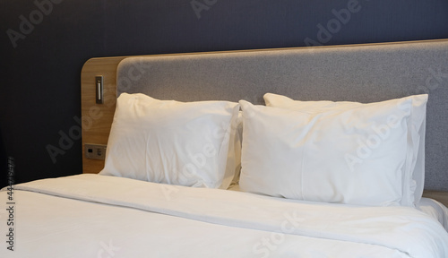 Close-up fragment of bedroom with empty bedside table, reading lamp and USB socket in modern interior​ design home or hotel. Soft pillow and blanket, stylish comfortable furniture.