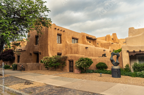 Pueblo Revival Style building with earth tone color, rounded corners and battered walls under dramatic cloudy sky, side, New Mexico Museum of Art, Santa Fe, New Mexico