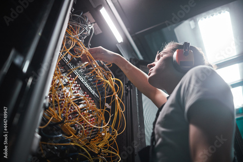 Low angle portrait of network engineer connecting cables in server room during maintenance work in data center, copy space