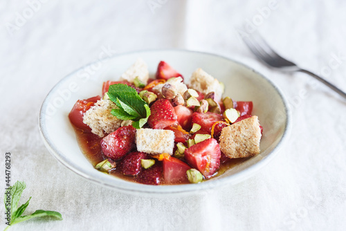Delicious summer salad. Salad bowl with strawberries, tomatoes, pistachios and croutons in honey orange oil sauce on beige linen tablecloth