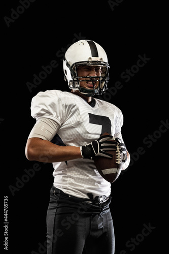 Portrait young American football player, athlete in black white sports uniform posing isolated on dark studio background. Concept of professional sport, championship, competition.