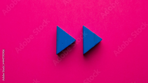  blue wooden triangles simulating rewind symbol on pink background