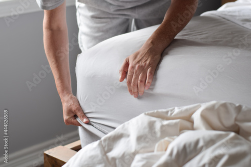 Woman is putting on a fitted sheet on a mattress while making the bed