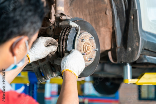 Car mechanic hands replace brakes in garage. Mechanic technician worker installing car wheel at maintenance. Worker changing brake disc in auto repair service center