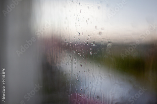 Rainy day through the window on cloudy grey sky and city buildings background. Concept. Evening cityscape behind the glass window with trickling drops of water.