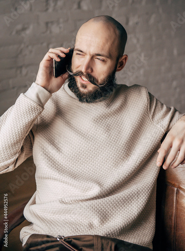  young bald man with a beard is talking on the phone in the room