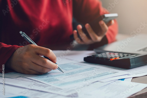 Close up woman using a pen filling form of Individual Income Tax Return, in living room at home.Expenses, account, taxes, home budget concept