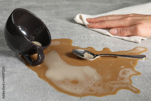 Woman wiping spilled coffee on grey table, closeup