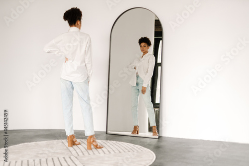 Young black woman standing and looking at mirror indoors