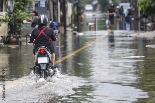 An unidentified woman riding a scooter through a flooded street.