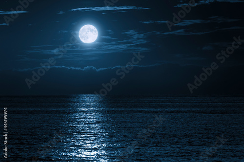 This large full blue moon rises brightly over the cloud bank in this calm ocean