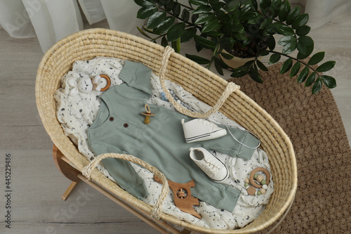 Cute baby clothes and accessories in basket bassinet at home, top view